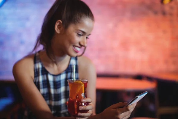 Junge Frau benutzt Handy beim Cocktailtrinken — Stockfoto