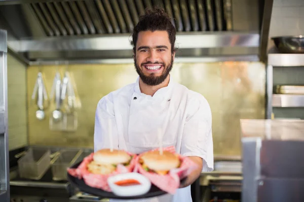 Kuchař, drží hamburgery v deska v kuchyni — Stock fotografie