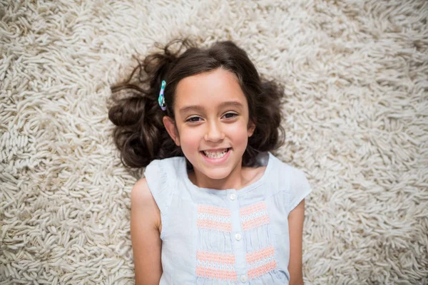 Sorrindo menina deitada no tapete na sala de estar — Fotografia de Stock