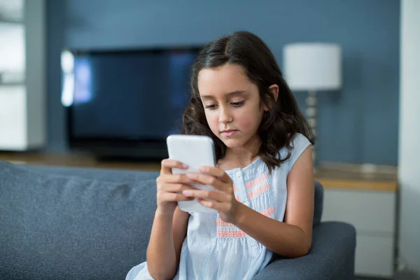 Unhappy girl sitting on sofa and using phone — Stock Photo, Image