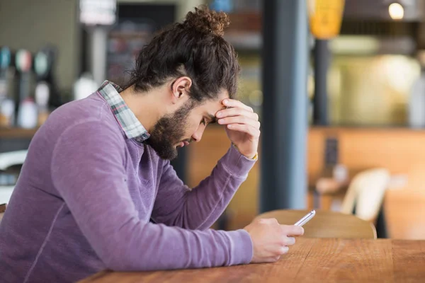 Depressed man holding phone in restaurant — Stock Photo, Image