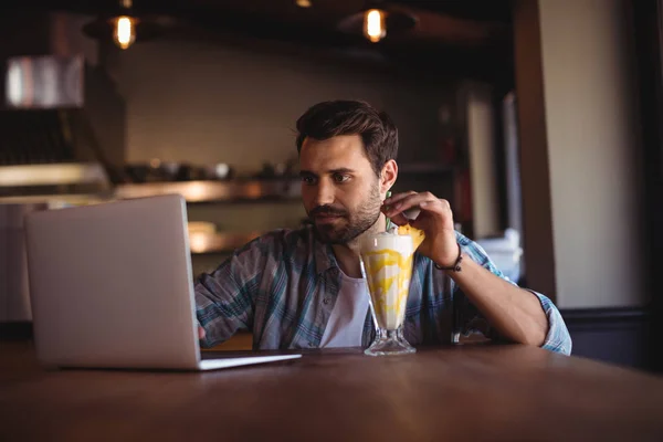 Homem usando laptop enquanto tem milkshake — Fotografia de Stock