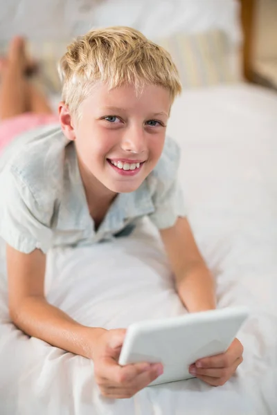 Niño sonriente con tableta digital acostado en la cama —  Fotos de Stock