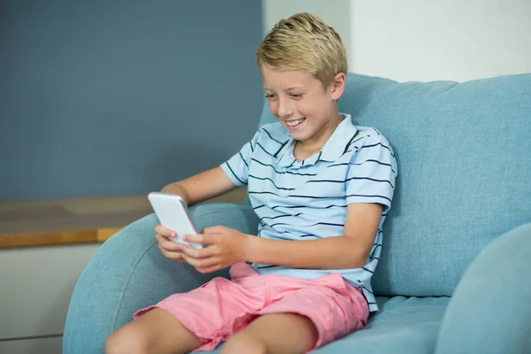 Хлопчик сидить на дивані і використовує телефон — стокове фото