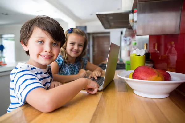 Irmãos usando laptop na cozinha — Fotografia de Stock