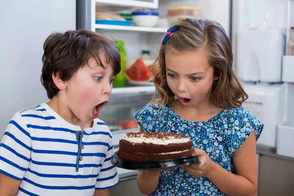 Surprised siblings looking at cake in kitchen — Stock Photo, Image