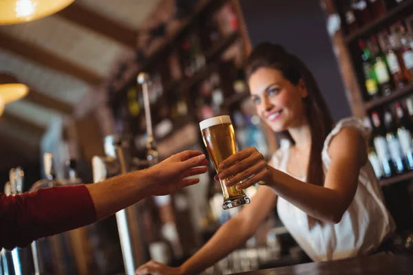 Vrouwelijke bar tender glas bier geven aan klant — Stockfoto