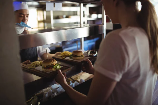 Chef pasando bandeja con papas fritas y hamburguesa a camarera —  Fotos de Stock