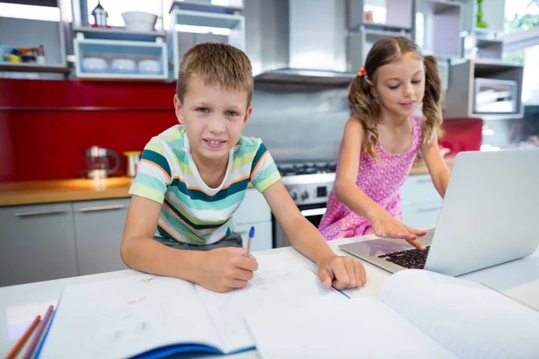 Pojken gör sina läxor medan flickan med laptop — Stockfoto