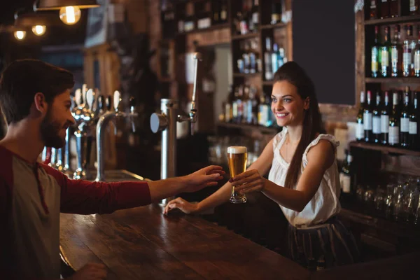 Female bar tender giving glass of beer to customer — Stock Photo, Image