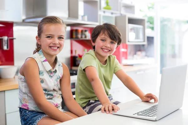 Smiling siblings using laptop in kitchen — Stock Photo, Image