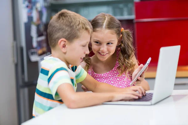 Fratelli che utilizzano laptop e telefono cellulare in cucina — Foto Stock