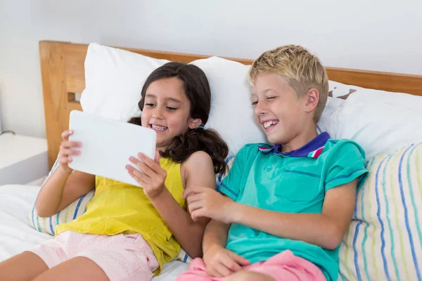 Hermanos usando tableta digital en la cama en el dormitorio —  Fotos de Stock