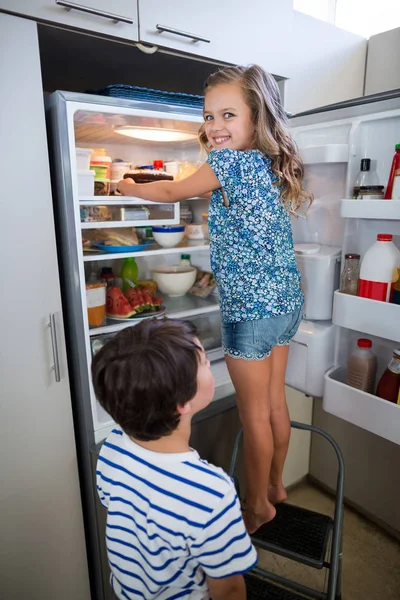 Siblings removing cake from refrigerator — Stock Photo, Image