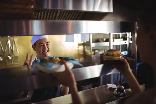 Chef pasando bandeja con papas fritas y hamburguesa a camarera —  Fotos de Stock