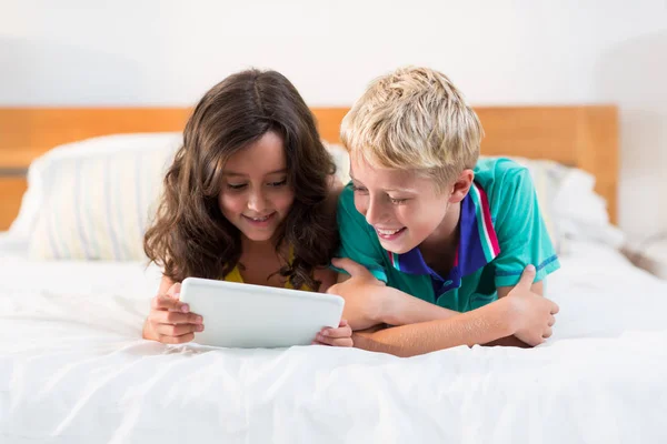 Smiling siblings using tablet on bed in bedroom — Stock Photo, Image