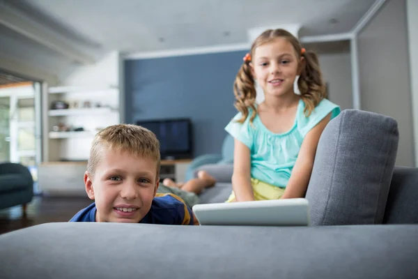 Siblings with digital tablet sitting on sofa — Stock Photo, Image