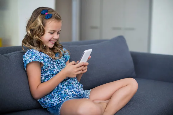 Fille assise sur le canapé et en utilisant le téléphone — Photo