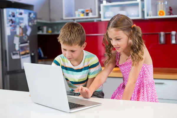 Irmãos usando laptop na cozinha — Fotografia de Stock