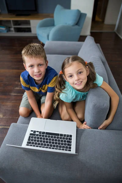 Fratelli e sorelle con computer portatile seduti sul divano in soggiorno — Foto Stock