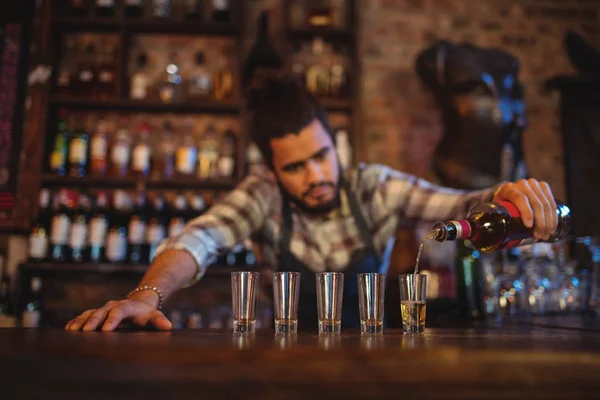 Camarero vertiendo tequila en vasos de chupito en el mostrador —  Fotos de Stock