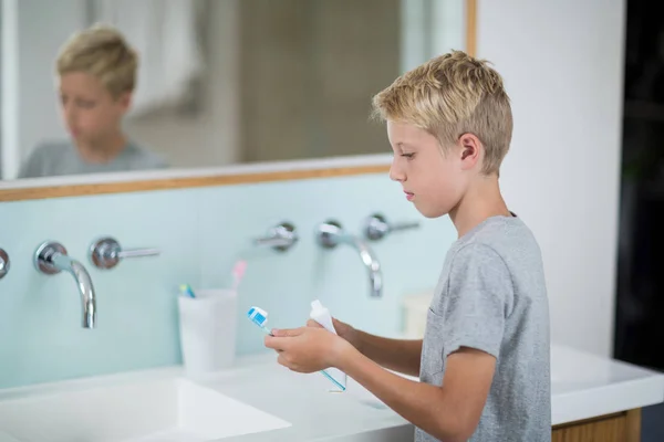 Jongen zetten tandpasta op de borstel in badkamer — Stockfoto