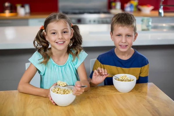 Lachende broer/zus met ontbijtgranen in keuken — Stockfoto