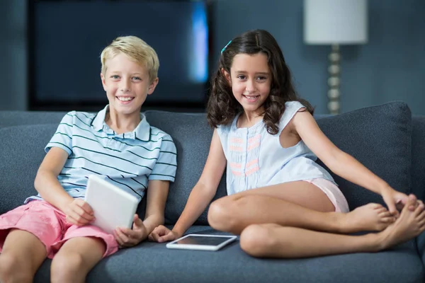 Frères et sœurs assis sur un canapé avec tablette dans le salon — Photo