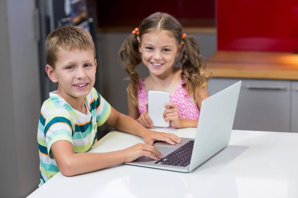 Sorridenti fratelli utilizzando il computer portatile in cucina — Foto Stock