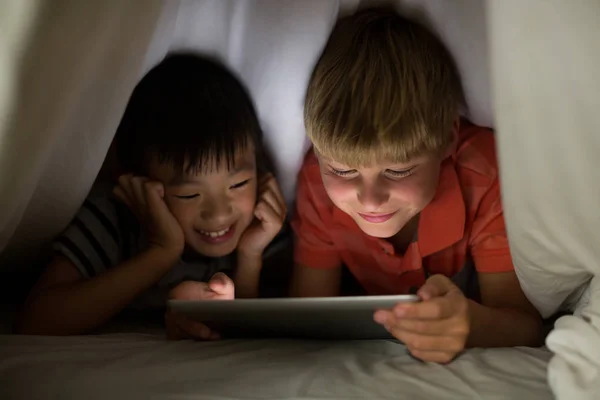 Siblings under bed sheet using tablet — Stock Photo, Image