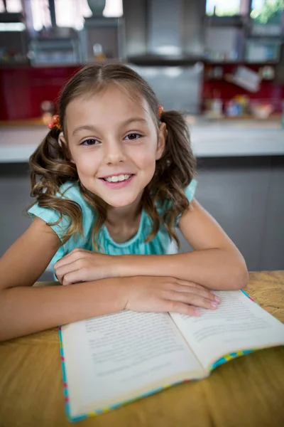 Усміхнена дівчина з книгою на кухні — стокове фото
