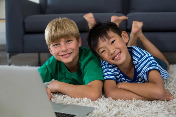 Irmãos sorridentes com laptop deitado no tapete — Fotografia de Stock