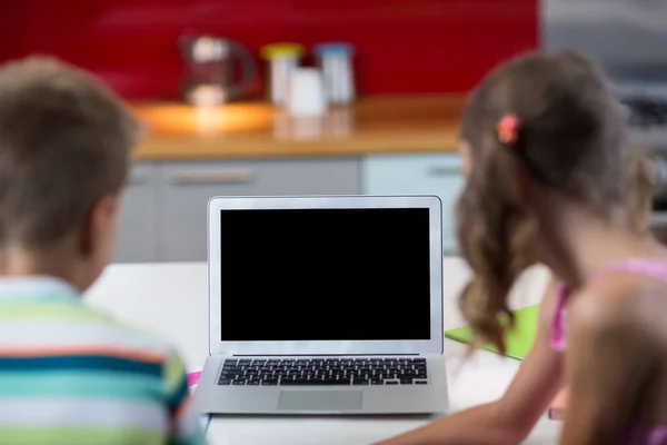 Lachende broers en zussen met laptop in de keuken — Stockfoto