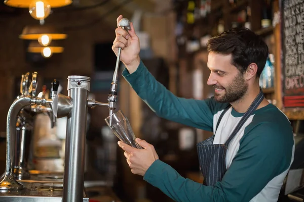 Happy bartender pouring beer from tap — Stock Photo, Image