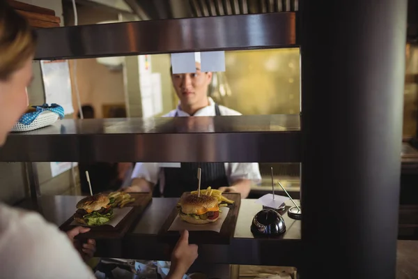 Chef passant plateau avec frites et hamburger à la serveuse — Photo