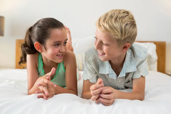 Hermanos sonrientes acostados en la cama en el dormitorio — Foto de Stock