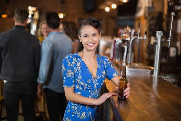 Mujer sonriente sosteniendo botella de cerveza en el pub — Foto de Stock