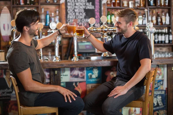 Male friends toasting beer mugs in bar — Stock Photo, Image