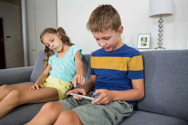 Siblings using tablet on sofa in living room — Stock Photo, Image