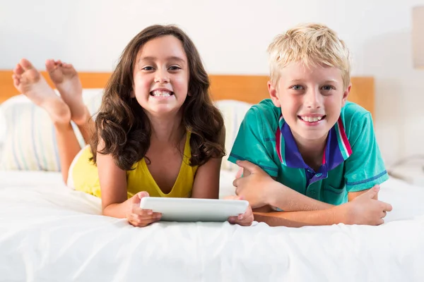 Hermanos con tableta digital acostados en la cama —  Fotos de Stock