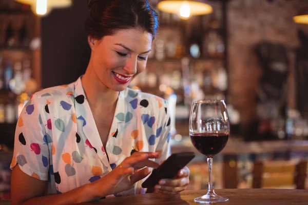 Vrouw met behulp van mobiele telefoon terwijl het hebben van wijn — Stockfoto