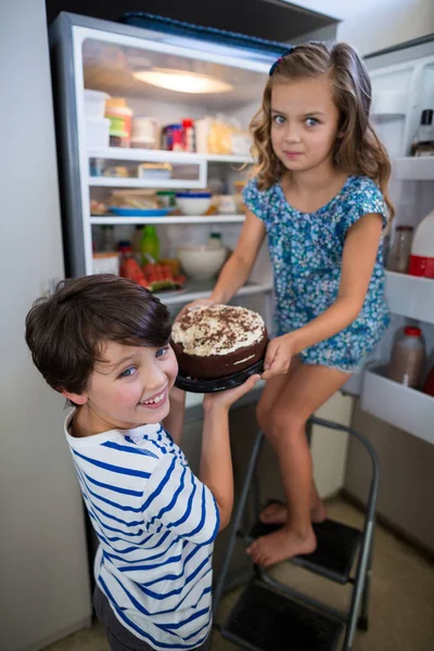 Los hermanos quitando la torta del refrigerador en la cocina — Foto de Stock