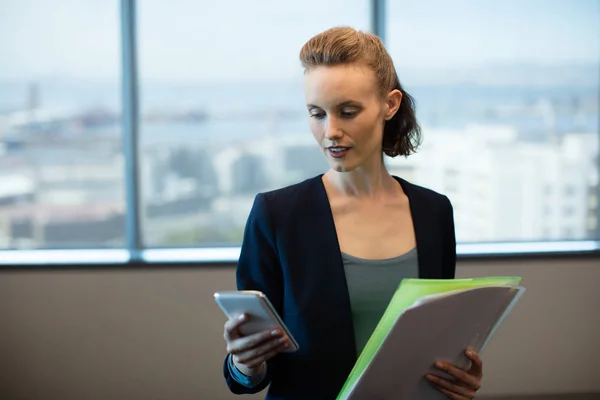 Businesswoman using phone while holding files — Stock Photo, Image