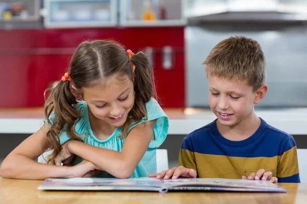 Siblings looking at photo album in kitchen — Stock Photo, Image