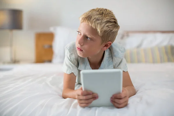 Ragazzo premuroso con tablet digitale sdraiato sul letto — Foto Stock