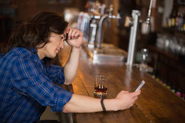 Deprimido jovem usando móvel no pub — Fotografia de Stock