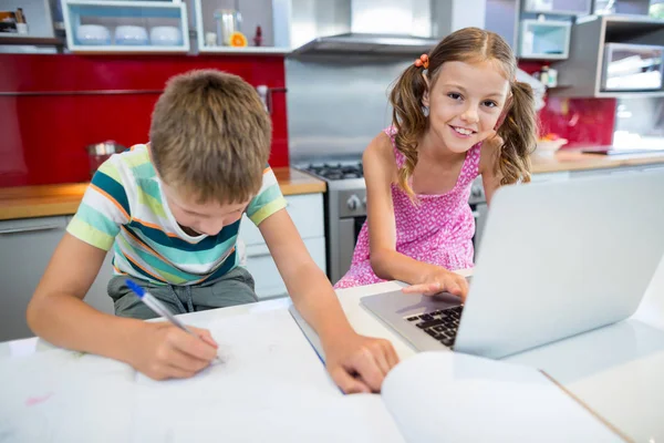 Boy doing his homework while girl using laptop — Stock Photo, Image