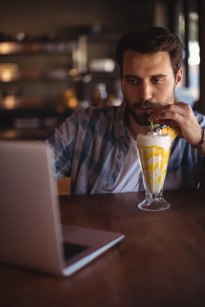 Homem usando laptop enquanto tem milkshake — Fotografia de Stock