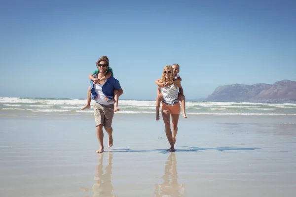 Pais piggybacking seus filhos na praia — Fotografia de Stock