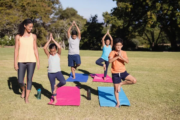 Entrenador mirando a los niños practicando Vriksasana — Foto de Stock